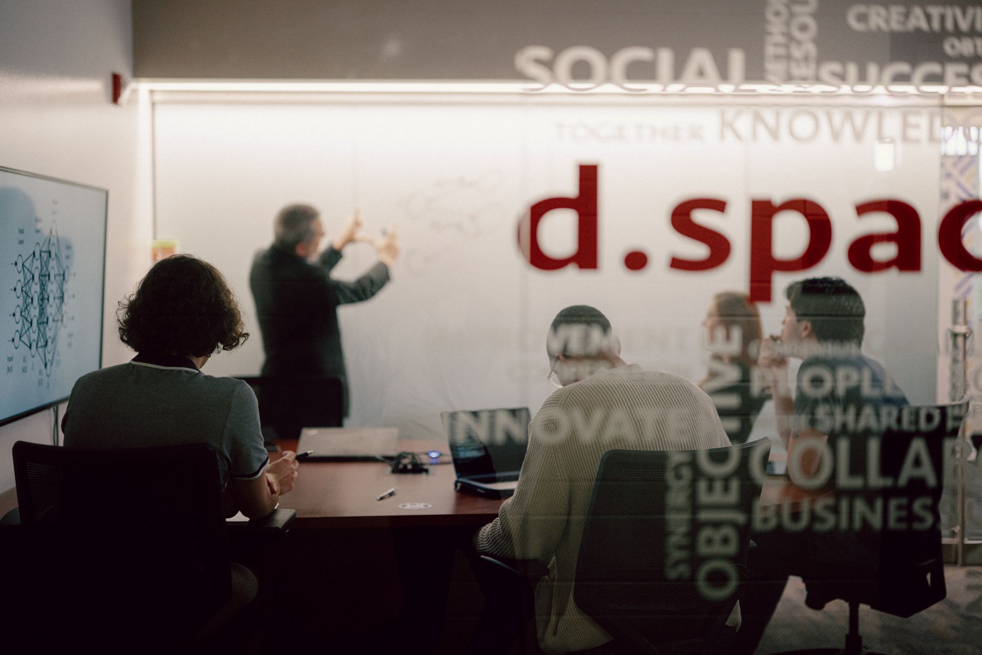 Lean Manufacturing master's students in a group meeting watching a professor write on a whiteboard in a classroom