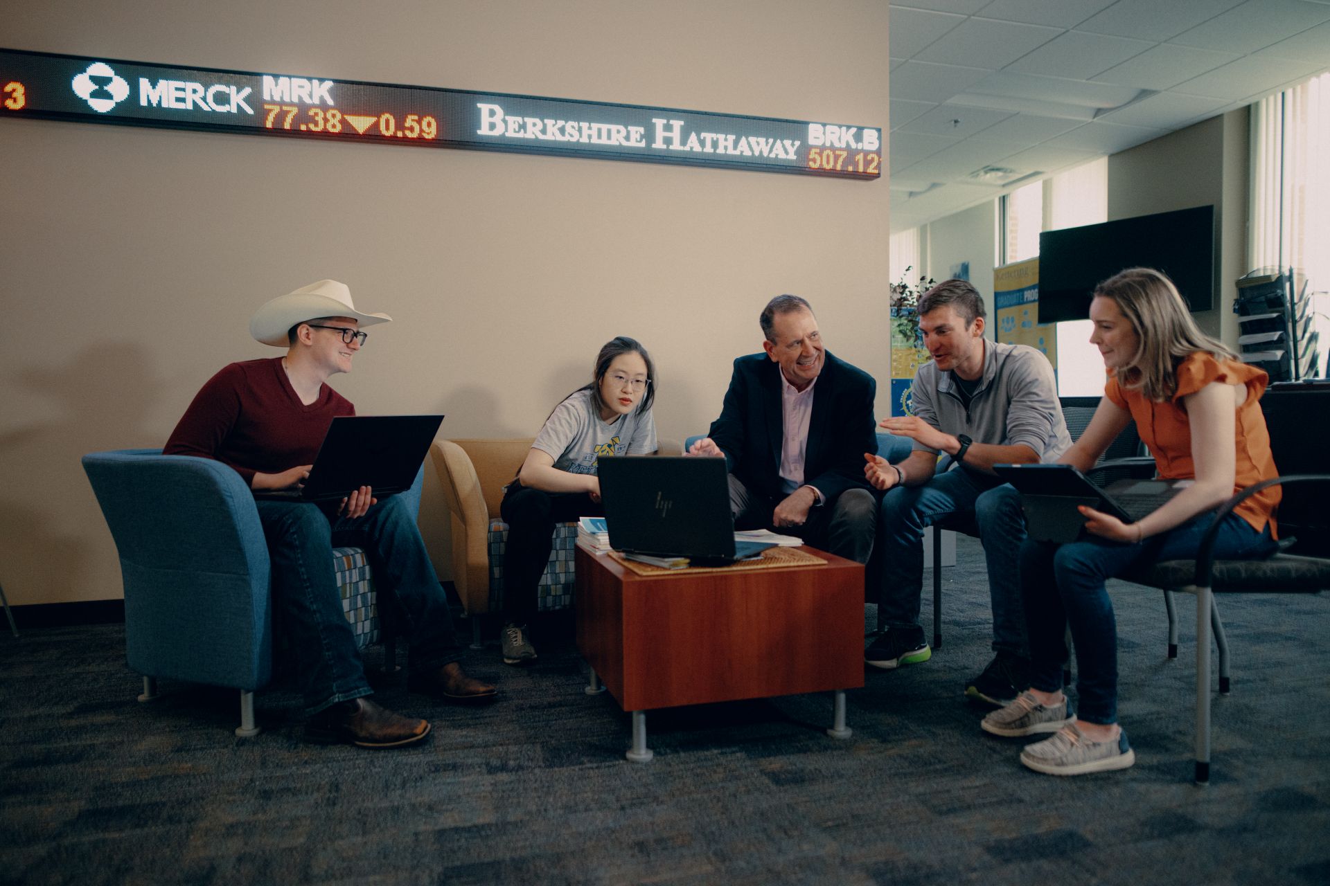 Operations Management master's professor and students discussing in a Kettering business lab with stock tickers