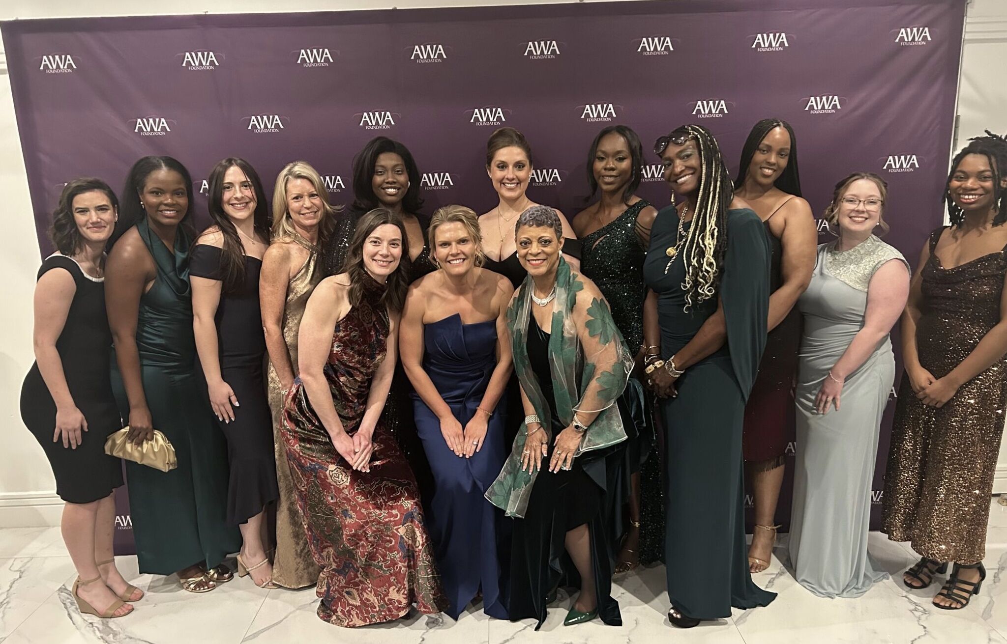 Female students in formal wear pose in front of a backdrop at the Automotive Women’s Alliance Foundation 30th Anniversary Gala.