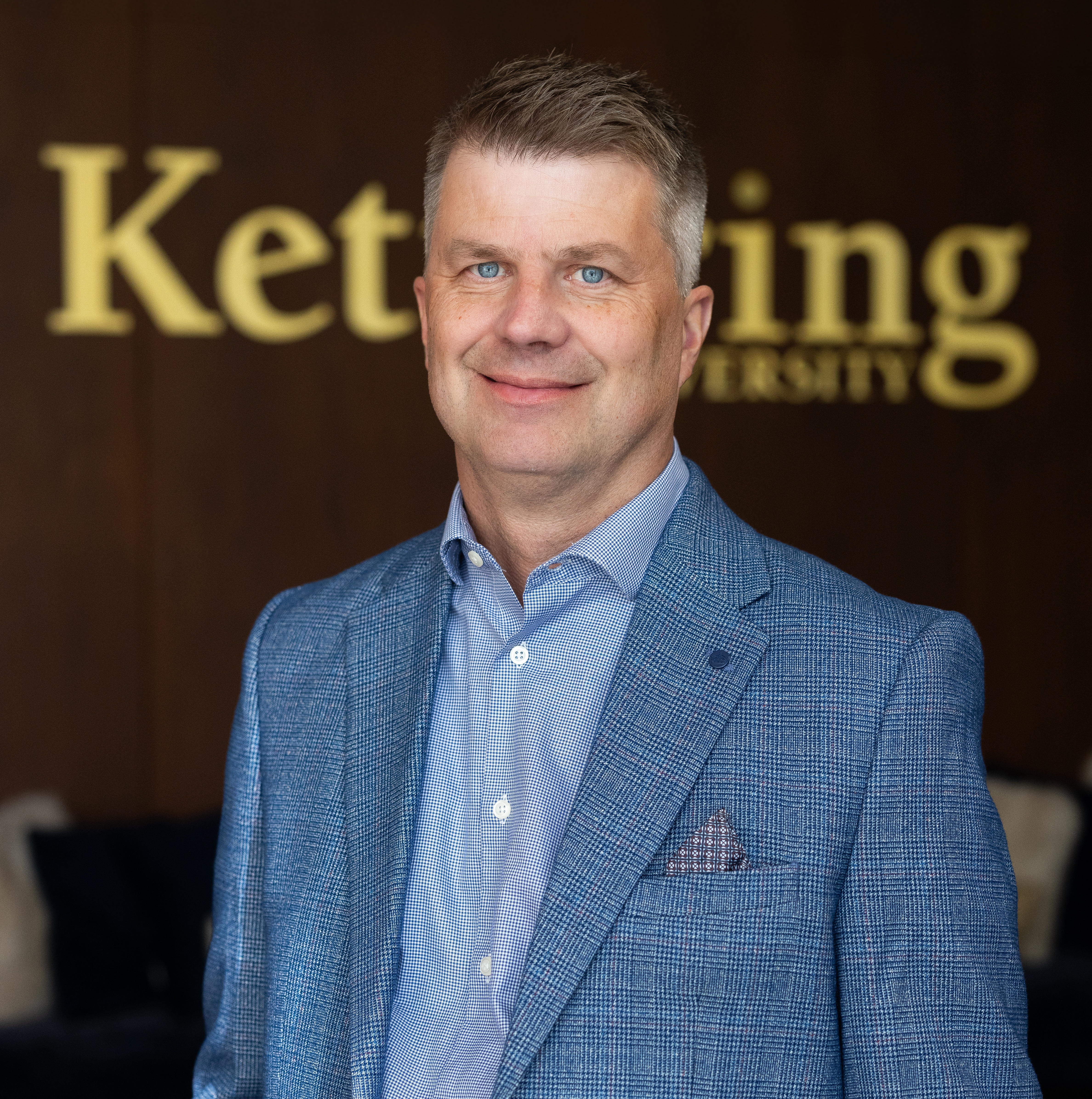 Dr. Scott Grasman stands in front of the Kettering University logo. 