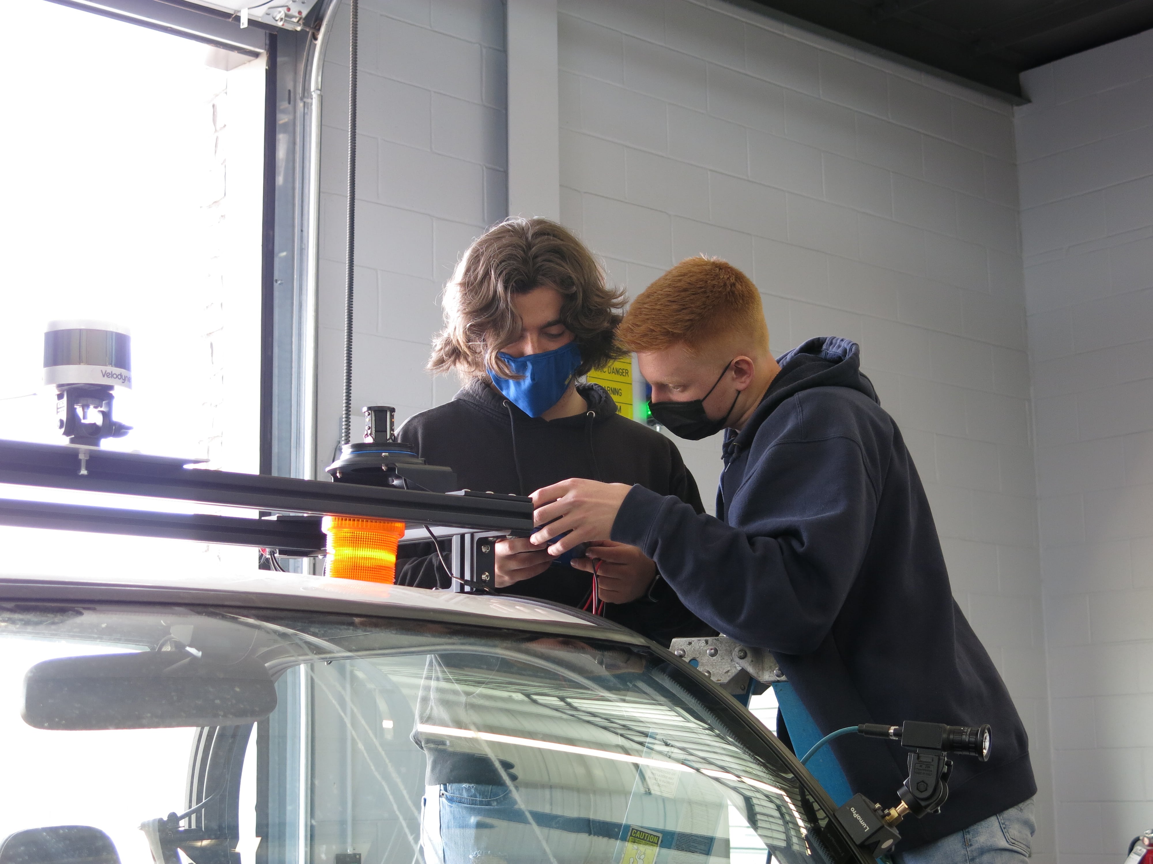 Two Kettering University students work on wiring on the roof of an intelligent ground vehicle.