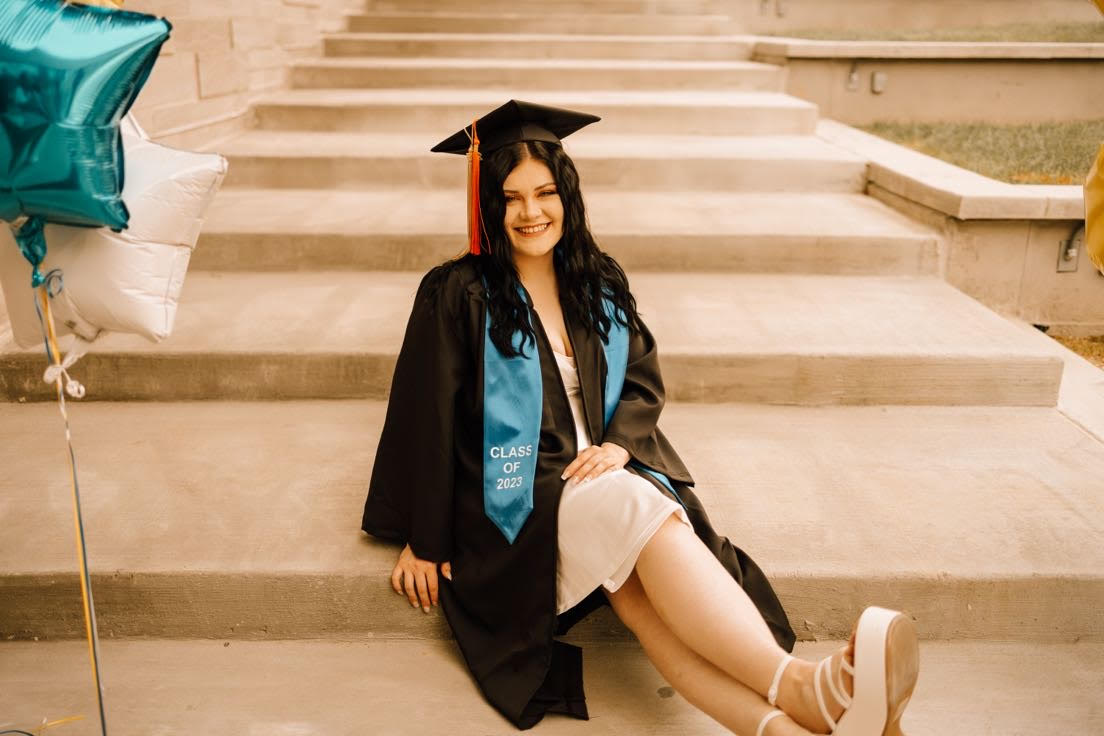 Olivia Wright sitting on steps in her cap and gown.