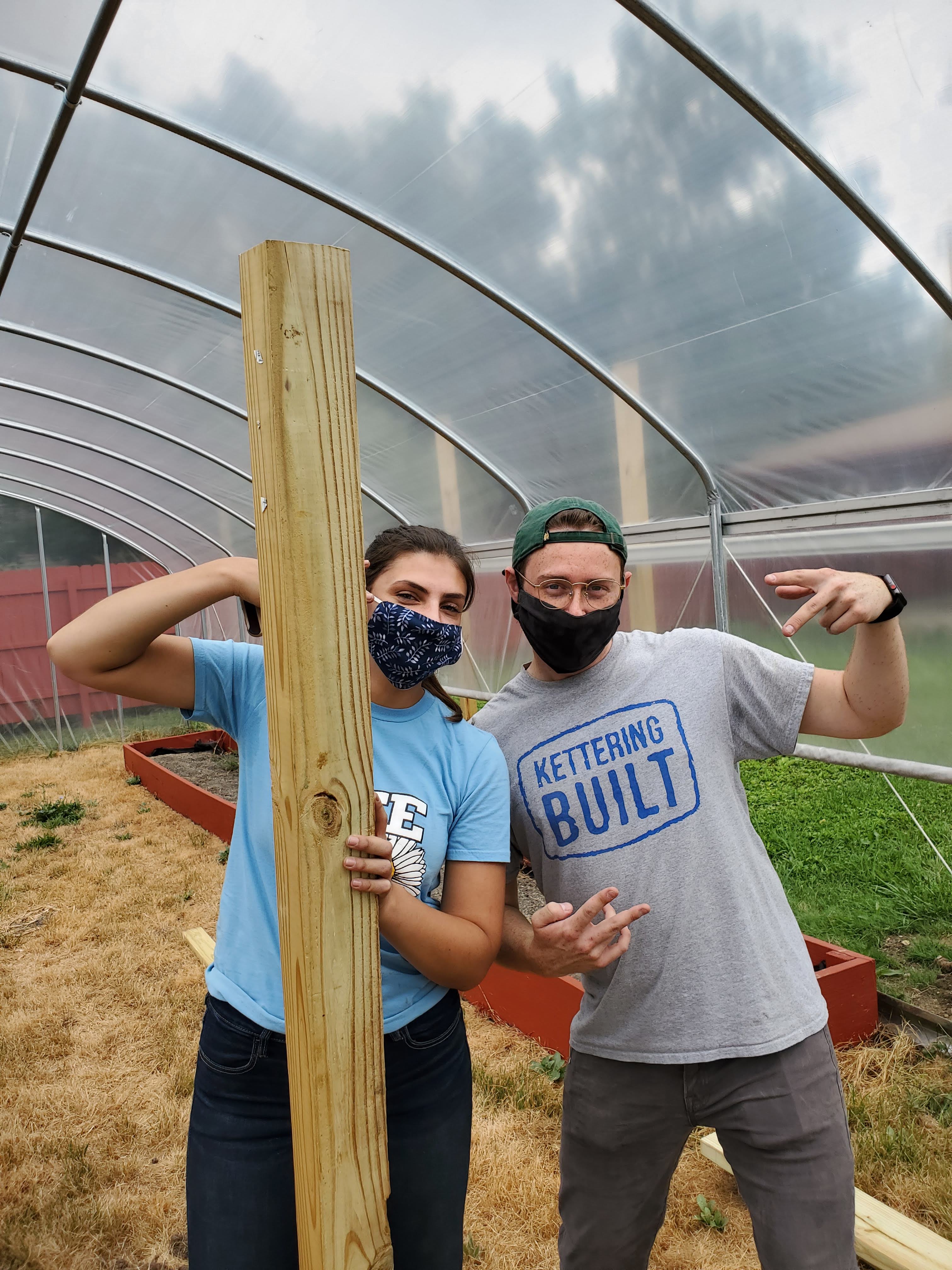 Two masked Kettering University students post inside the hoop house they helped design.