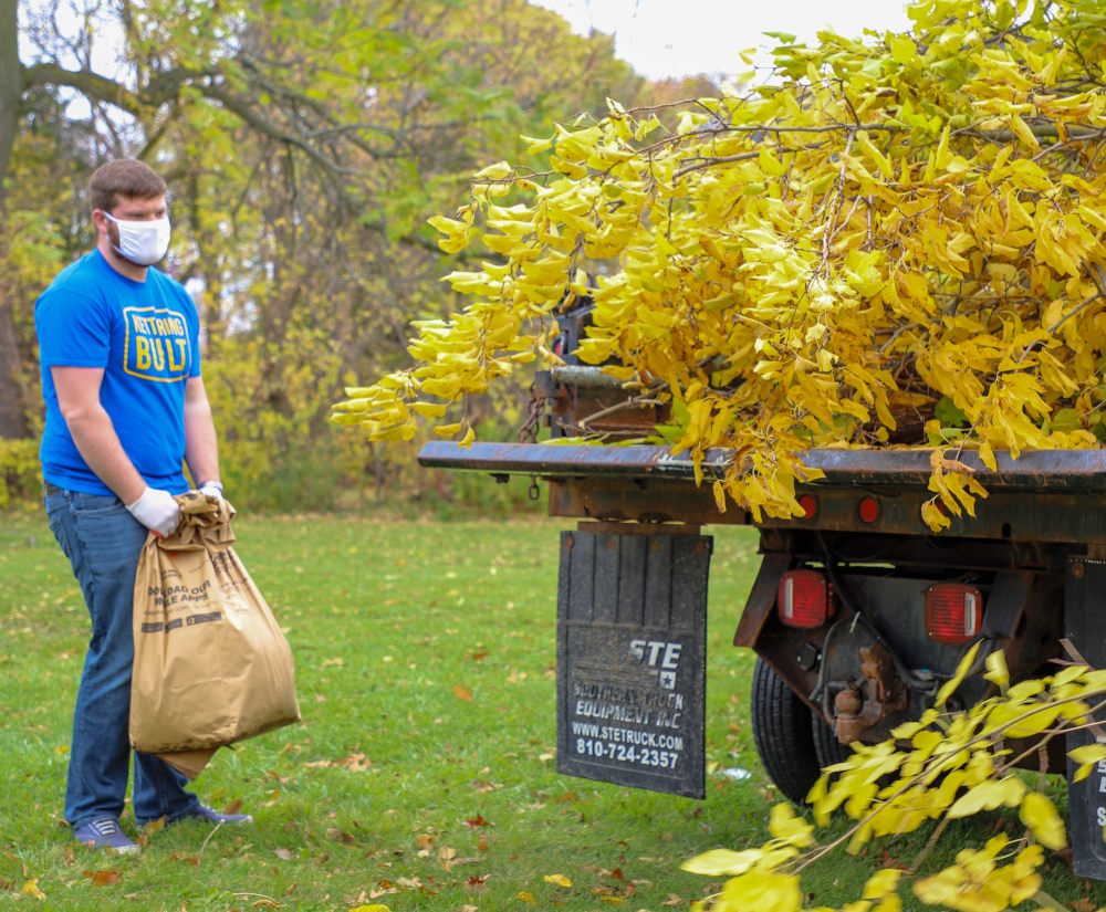 A Kettering University student hauls a bag of leaves to a truck.