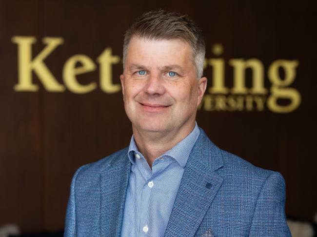Dr. Scott Grasman stands in front of the Kettering University logo. 