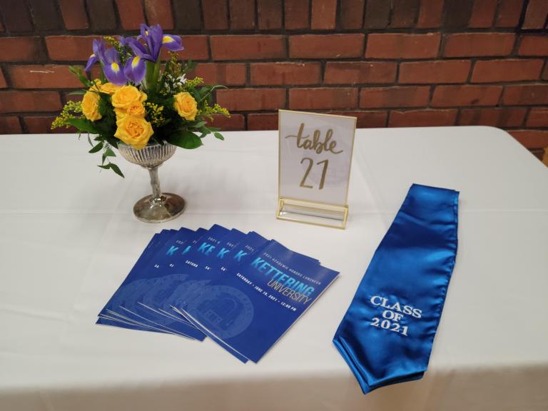 2021 Honors luncheon programs, a sash, table number card and flower centerpiece sit on a table.
