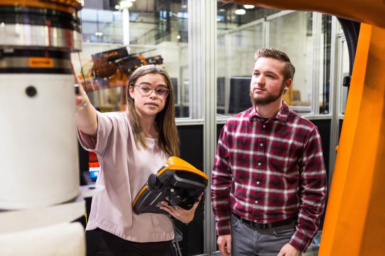 Two Kettering University students, a female and a male, look at a large piece of machinery.