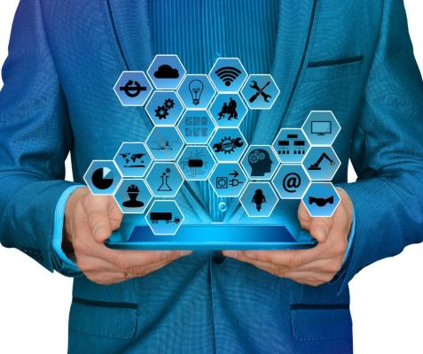 A man holds a tablet with an image popping out of different hexagons. Each hexagon has a different symbol in it such as a lightbulb, pie chart, brain, beaker or tools.