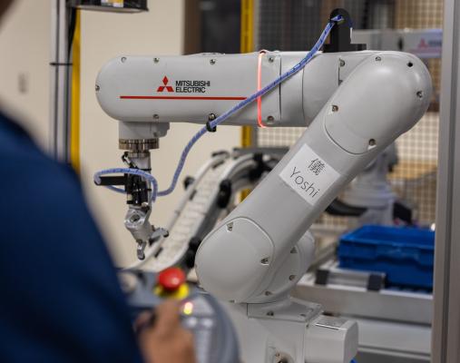 A robotic arm with a person in the foreground, out of focus, controlling it. 