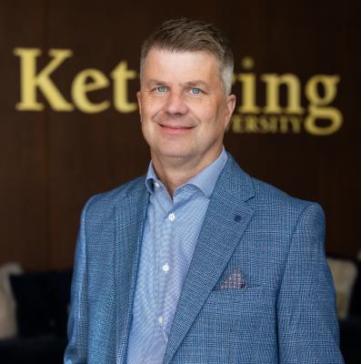 Dr. Scott Grasman stands in front of the Kettering University logo. 