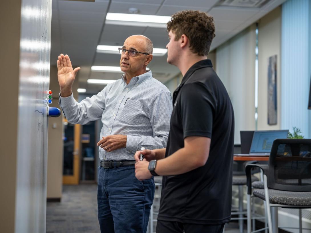 A School of Management Kettering professor explains a business concept to a student in front of a whiteboard