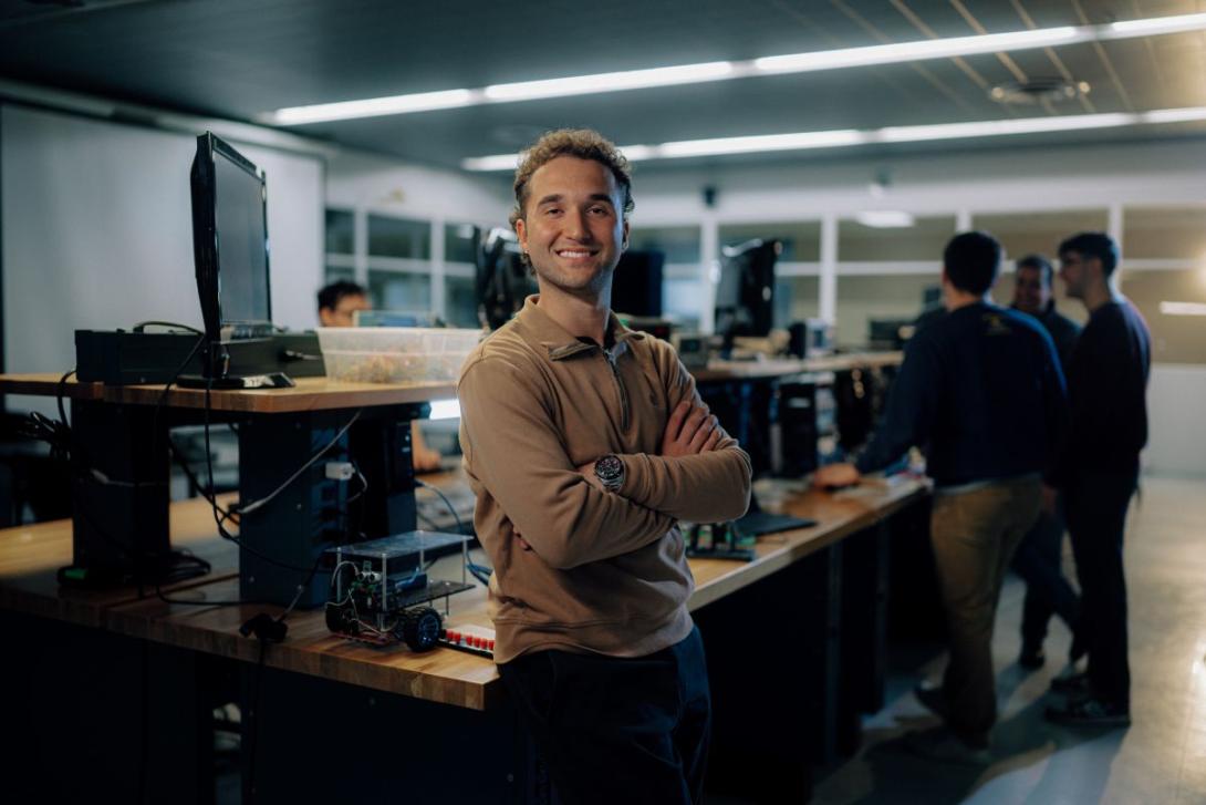 Smiling Electrical and Computer Engineering master's student standing in an engineering lab with computers and equipment