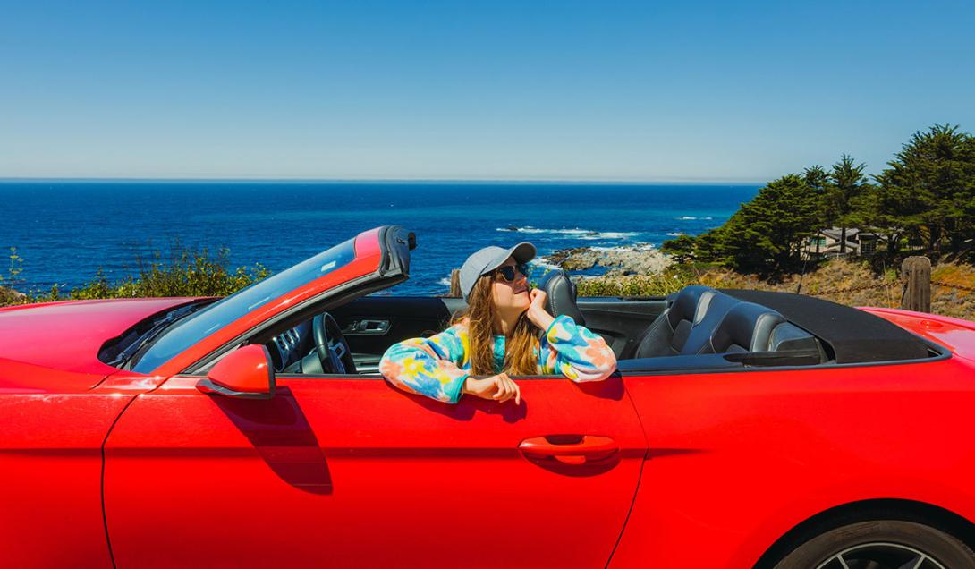 Young girl driving a red convertible next to the ocean