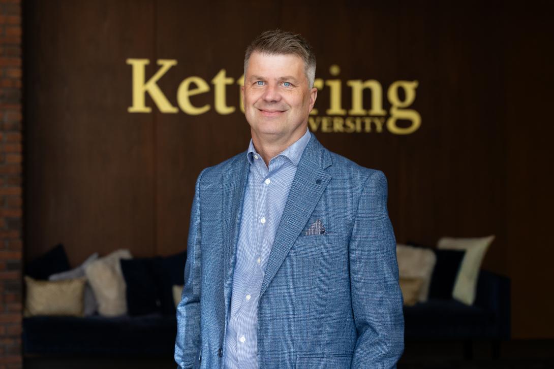 Dr. Scott Grasman stands in front of the Kettering University logo. 